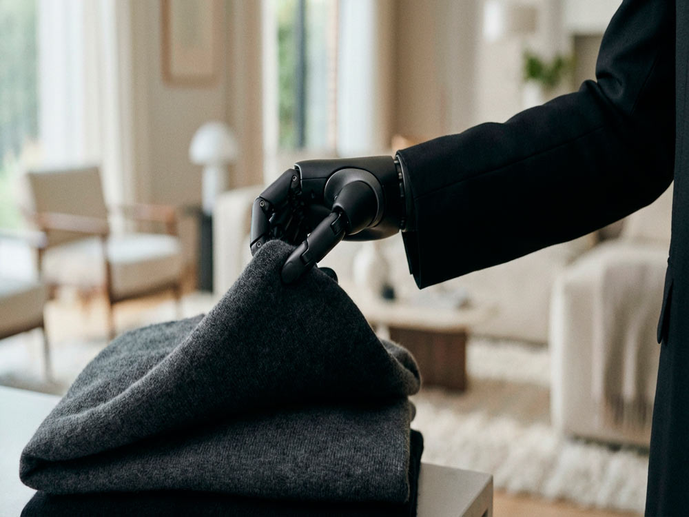 Рука гуманоїдного робота 1X Neo піднімає одяг у домашній обстановці